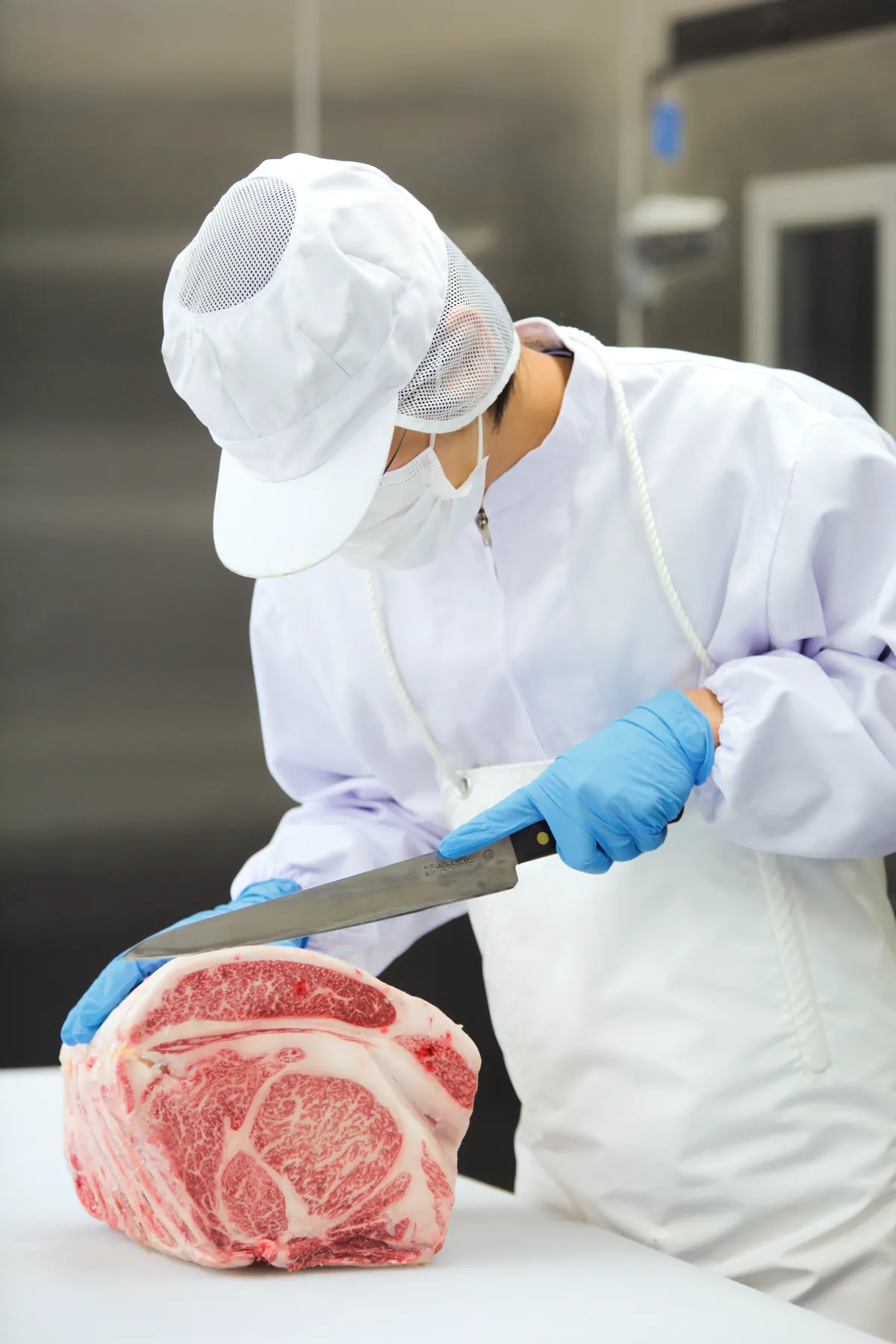 衛生服を着た作業員が牛肉ブロックを包丁で整形する様子